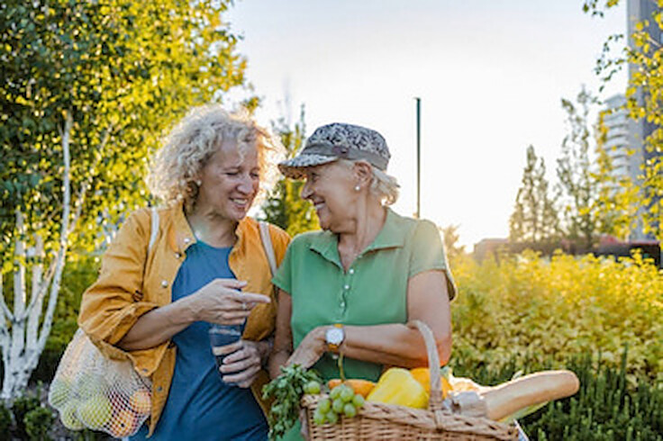 Two older women smiling as they walk home with bags of fresh groceries