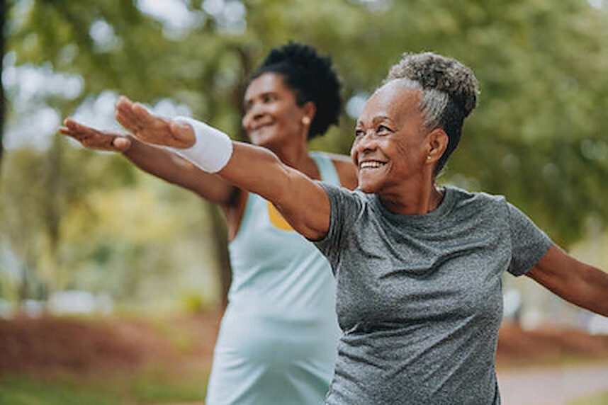 Two women smiling as they stretch their arms wide during an outdoor exercise session