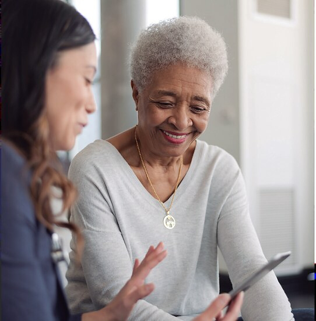 A caregiver showing a smiling older woman something on a tablet