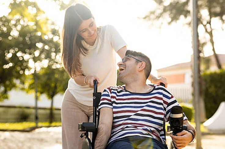 A support worker sharing a laugh with a young man in a wheelchair outdoors