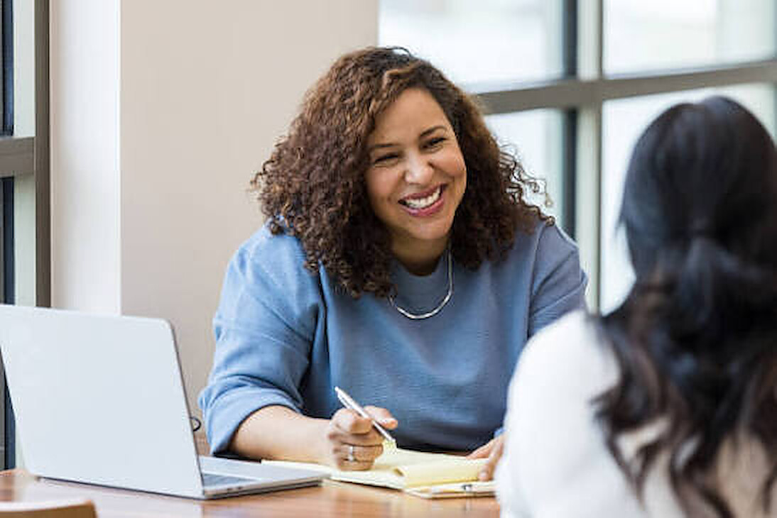 A smiling hiring manager taking notes during a friendly interview at a sunny desk