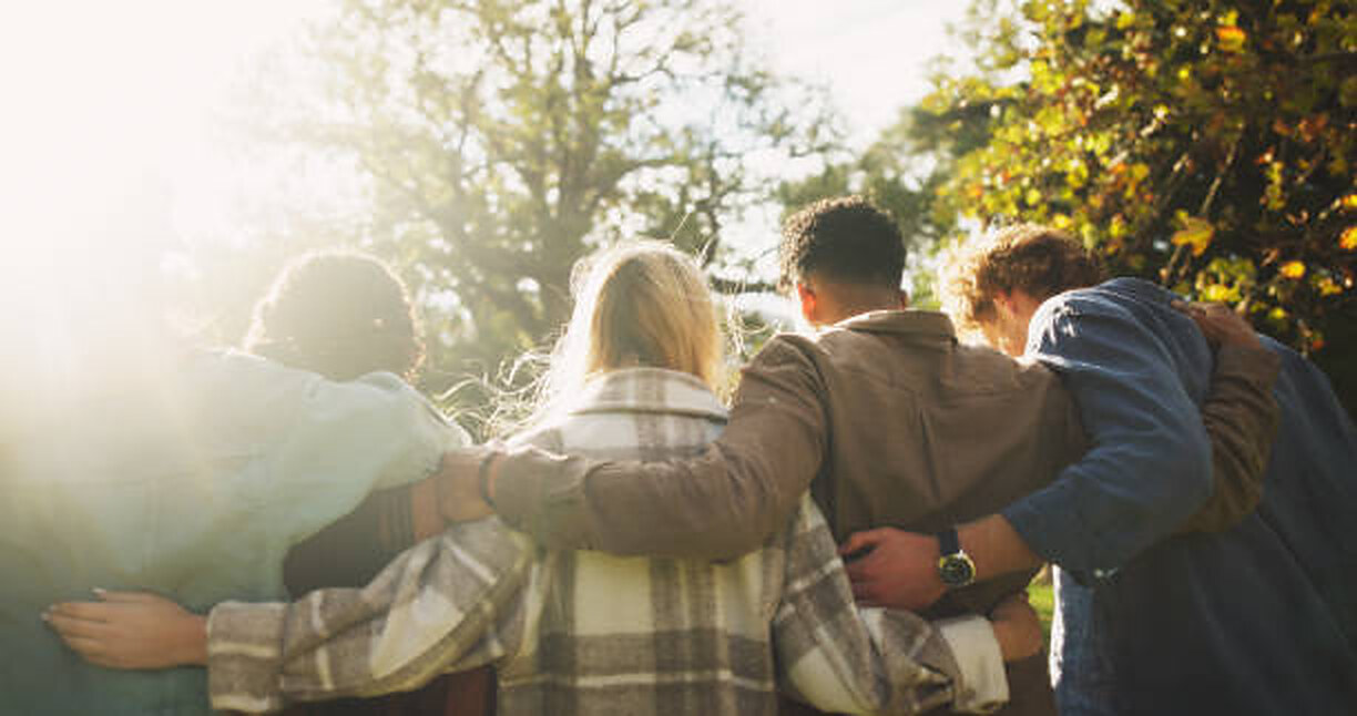 A group of friends walking arm in arm through a sunlit park