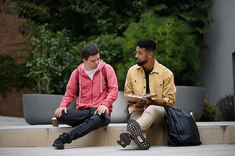 A young man with Down syndrome talking with a support professional as they sit together outdoors